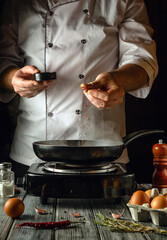 In a cozy kitchen, a skilled chef adds a pinch of seasoning to a frying pan with eggs. The warm, inviting atmosphere highlights the art of cooking as aromas fill the air