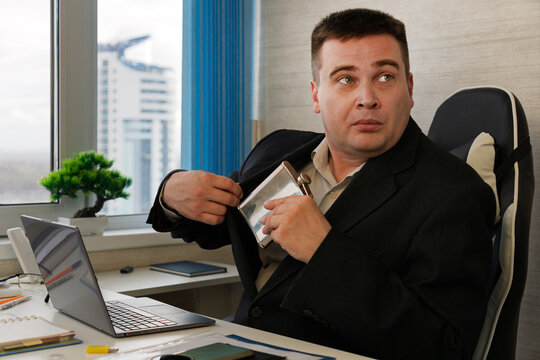The man hides a flask of rum in his jacket pocket.. Businessman looking scared while taking a hip flask out of his jacket at work, hiding alcohol addiction issues of alcoholism in the workplace