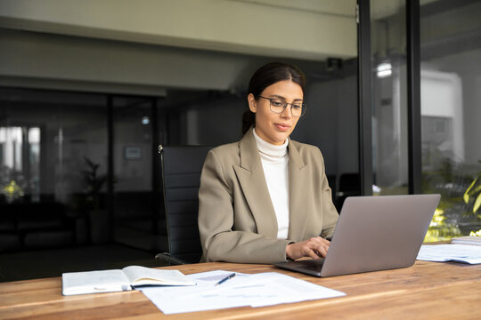 Smiling young middle eastern business woman specialist working focused on laptop computer. Middle aged latin hispanic investor, bank worker using pc for analysing, network at workplace desk in office