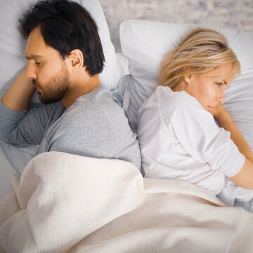Unhappy sad couple, family beard man, woman, husband, wife lay in bed, turn away back to back. Unlove crisis, sexual problem issues relationship conflict divorce concept. Brick wall background. Square