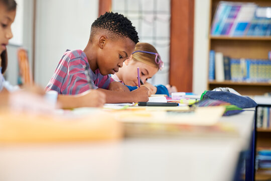 Children sitting in a row in classroom doing homework in primary school - Powered by Adobe