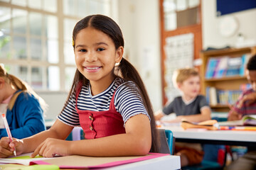 Portrait of happy hispanic girl looking at camera in elementary classroom