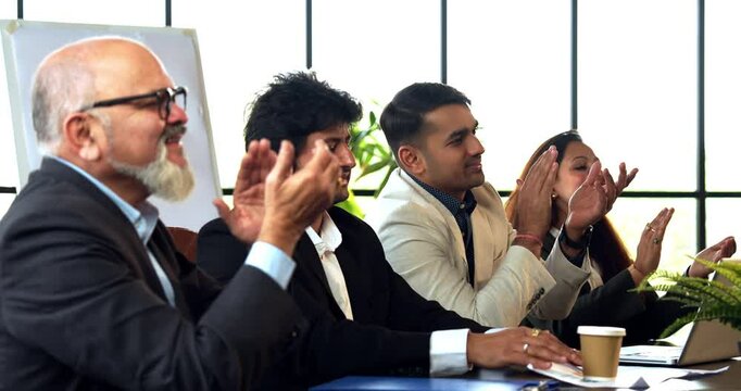 Indian Asian group of four successful business people in executive attire, clapping and looking at someone sitting across the conference table