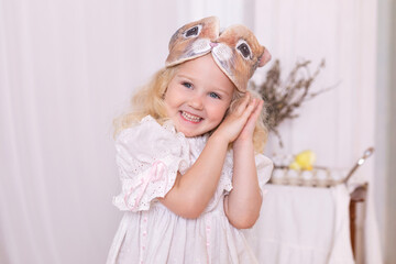 Happy smiling fun little blond curly hair girl with rabbit ears mask on the head on Easter at home. Closeup Portrait Happy cute child girl with bunny ears enjoying good mood. Vintage style