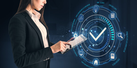 Businesswoman using a tablet with futuristic holographic checkmark interface on a dark background.