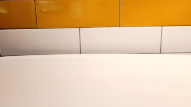 White male hand picking up house and car keys from a white table before throwing them down again. The background is a yellow and white brick wall.