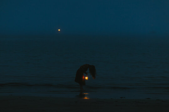 Anonymous woman with lantern on moonlit beach