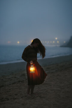 Woman holding a lantern on a beach at dusk