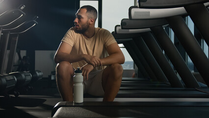 Tired African American man sit on treadmill relax after hard physical workout cardio training in...