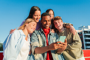 A joyful group of diverse friends enjoying a moment together outdoors, smiling and using a...