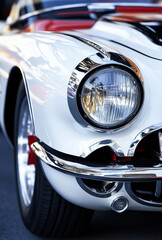 A vintage white car with chrome accents is parked on a bustling city street