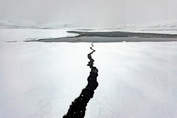 Cracked ice surface in Greenland  revealing dark waters beneath in a remote snowy landscape