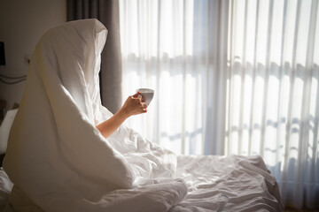 Woman with cup of coffee in the morning under the blanket at home