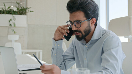 Busy Arabian Indian muslim man successful entrepreneur employer CEO boss leader executive manager businessman talking mobile phone in office workplace using laptop consult client business discussion