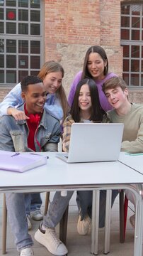 Vertical. Group of enthusiastic students gathered around a laptop, engaged in collaborative study session, sharing ideas and excitement, teamwork and learning among teenagers at university campus