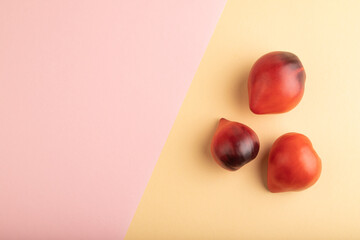 Red Heart shape tomatoes on pink and orange pastel paper. Top view, copy space
