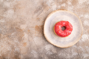 Pink Donut with sprinkles on blue ceramic plate on brown concrete, top view, copy space