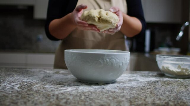 Woman placing bread dough into a bowl on a flour-dusted counter in a modern kitchen.
