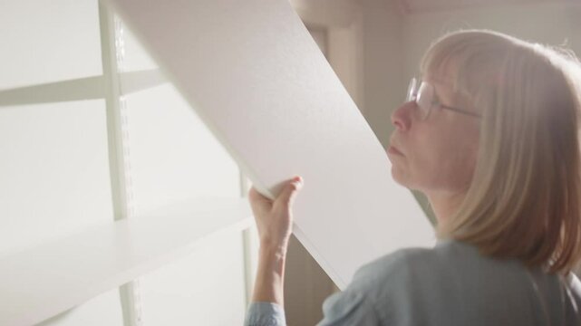 60 year old handywoman installs white shelving unit against wall, closeup