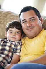 Fototapeta premium Loving Hispanic Father and Son Bonding on Couch While Watching Cartoon at Home