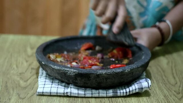 Indonesian woman's hands grinding spices on a stone mortar for sambal. Traditional Indonesian sambal being prepared with mortar and pestle. Asian womans hands crushing chili peppers and spices 