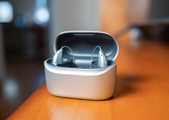 Hearing aid devices resting inside charging case on wooden table