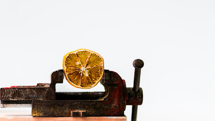 A dried orange slice held in a vintage metal vise against a white background. Minimalist still life concept symbolizing pressure, preservation, or creative contrast. Isolated studio shot.
