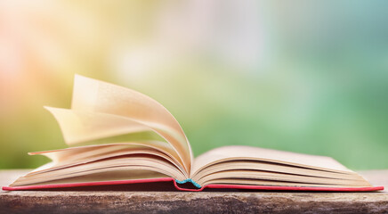 warm summer wind turns the pages of an open red-covered book lying on a wooden table. copy space