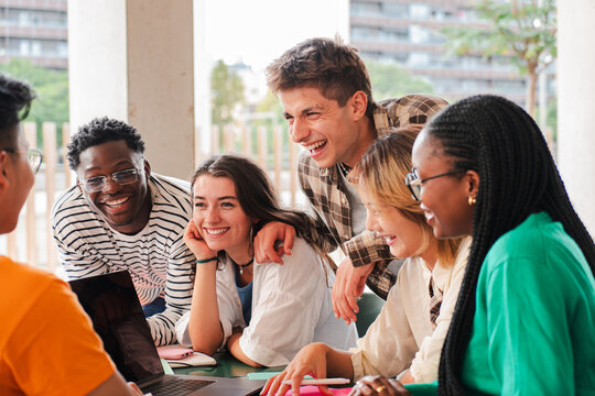 Big group of teenage students talking together sitting on a university campus bench. Young friends having fun on a social gathering outside. Classmates having a conversation on a friendly meeting