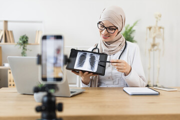 Middle Eastern female doctor records online lesson on lung X-ray diagnosis. Educating audience on respiratory health using digital tools.