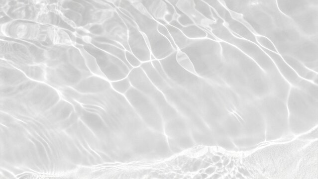 Closeup of desaturated transparent clear calm water surface texture with splashes and bubbles. Trendy abstract nature background. White-grey water waves in sunlight in a soft minimal aesthetic style