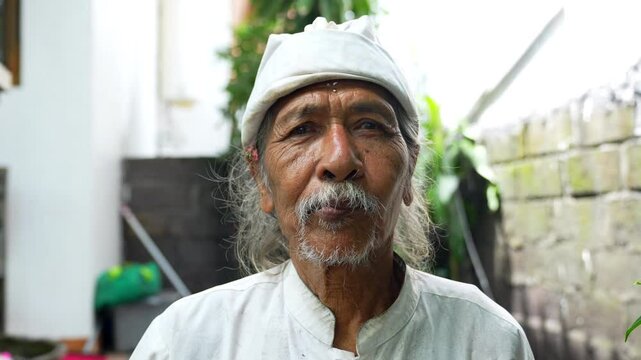 Portrait elderly man with a serene expression wearing a traditional white outfit and head covering, standing outdoors. Old man look at camera. His wrinkled face reflects wisdom and experience. 