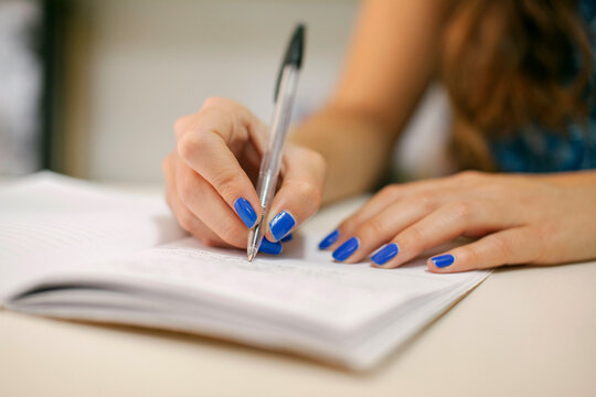 Person writing in notebook with a pen and manicured nails