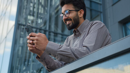 Indian Arabian man male entrepreneur worker smart businessman office manager hold mobile phone outdoors online chatting create business idea insight gesture texting message browsing smartphone in city