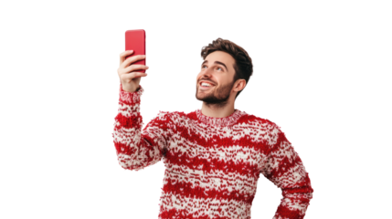 Cheerful young man in a festive sweater taking a selfie with a red smartphone, exuding joy in a playful moment.