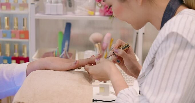 Asian nail spa owner painting customer&rsquo;s nails with precise brush strokes in a clean and well-organized spa. highlight professionalism and creative service in a small business setting.