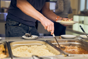An unrecognizable volunteer puts nutritious food on a plate in a modern charity canteen. High quality photo