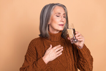 Elderly woman feeling relaxed and content while holding water glass against beige background