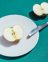 two halves of one apple, one half lies on a white plate with a table knife, the second next to it, an apple cut into halves