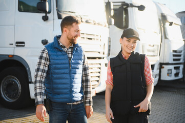 Two professional truck drivers stand in front of the big truck. They talk and perform a technical...
