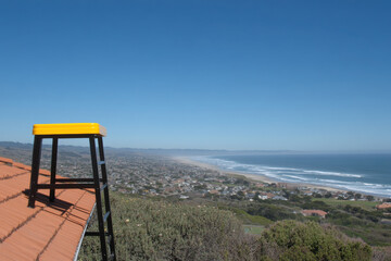 A yellow ladder is on a roof overlooking a beach and a city