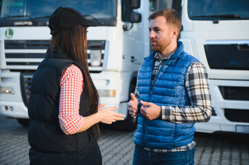 Two professional truck drivers stand in front of the big truck. They talk and perform a technical...