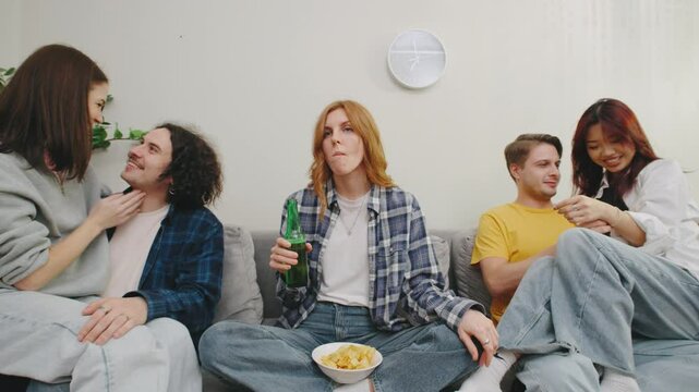 lonely girl sits in the middle and eats chips with beer, couples in love around. A closeknit group of friends gathers in a cozy and warm living room, filled to the brim with their laughter and