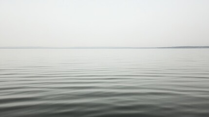 Obraz premium Calm lake water under a hazy sky.