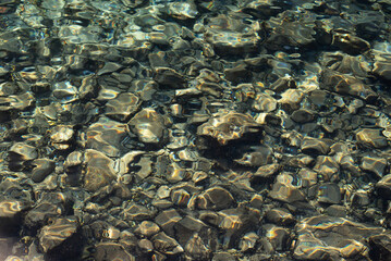 Sea rocky bottom under transparent blue water. Clear turquise lake surface rippled with sun ray reflection.