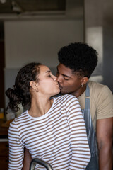 Obraz premium A loving couple shares a tender kiss in the kitchen, showcasing romance and intimacy, with a warm and cozy atmosphere in a casual home setting