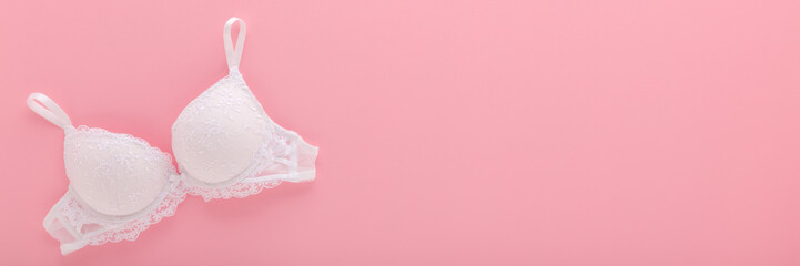 New white lace bra on light pink table background. Pastel color. Female casual underwear. Closeup. Empty place for text. Wide banner. Top down view.