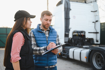 Logistics - proud driver or forwarder and female coworker, in front of trucks and trailers, on a...