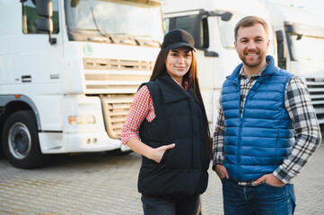 Logistics - proud driver or forwarder and female coworker, in front of trucks and trailers, on a...