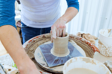 Hands expertly shape clay vase on potter wheel in bright studio setting.